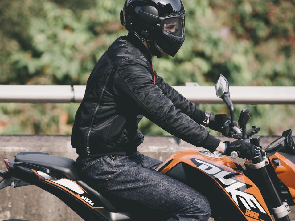 Astric moottoripyörätakissa on selkäsuojana kokoontaitettu moottoripyörän peite pakkauksineen. Takin voi myös jättää peitteen alle piiloon pyörältä poistuessaan.
