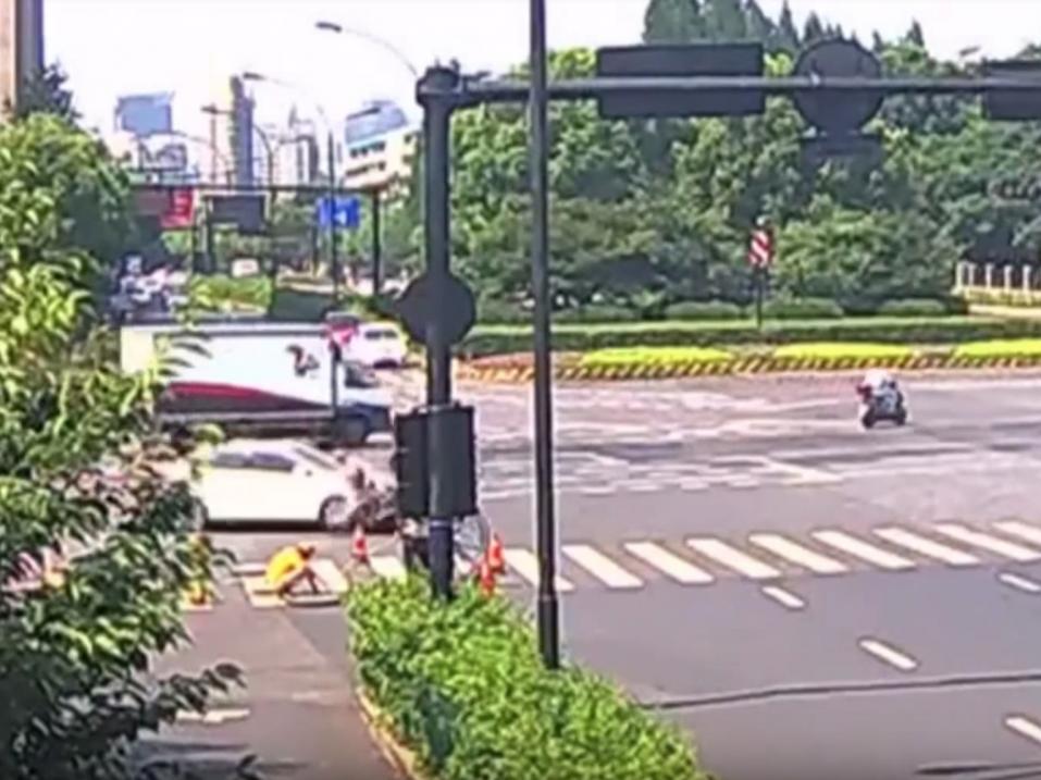 Tässä kuvassa näkyy tarkkaan katsottaessa, miten nainen on skoottereineen törmännyt valkoisen auton keulaan. Avoin tarkastuskaivo auton etupuolella.
