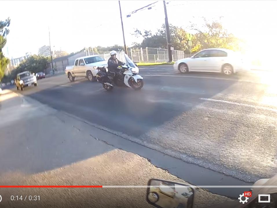 Poliisi auttamassa vasemmalle kääntyvää moottoripyöräilijää vilkkaan liikenteen keskellä.