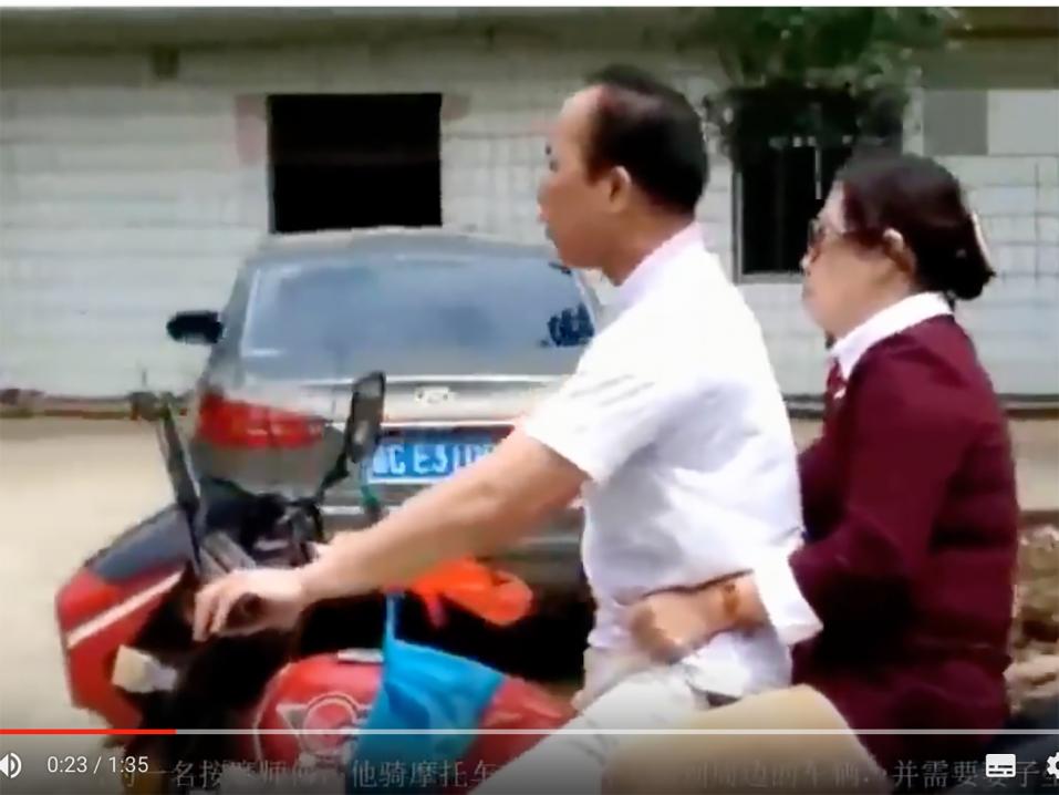 Sokea mies ajaa moottoripyörällä ja vaimo auttaa takapenkiltä.