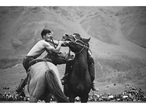 Tulpar Kol – KYRGYZSTAN 25 July 2015. Two men on horses participate in a wrestling competition during the National Horse Games Festival on the shore of Tulpar Kol.